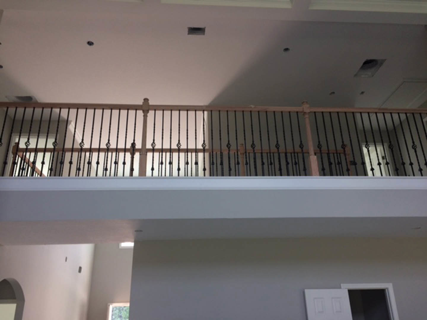 Wood staircase with black metal railing, white paneled door, white walls, and balcony overlooking open interior space