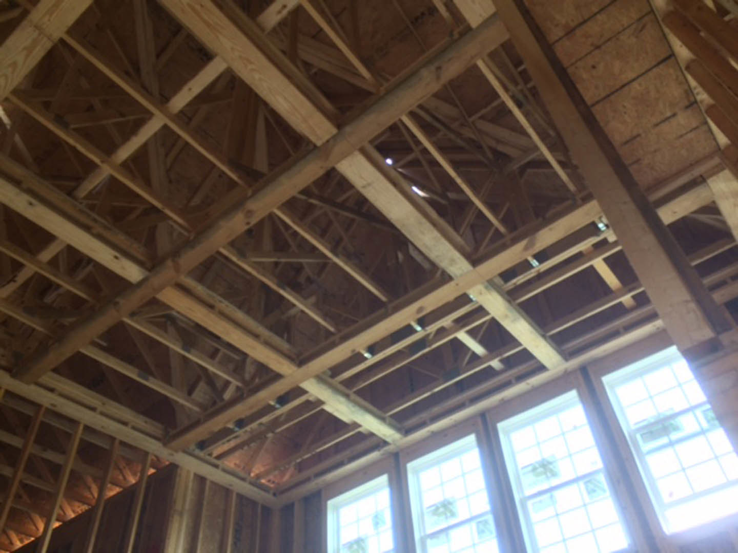 Exposed wood framing and beams surrounding a square-paned window with daylight streaming through, unfinished interior structure visible
