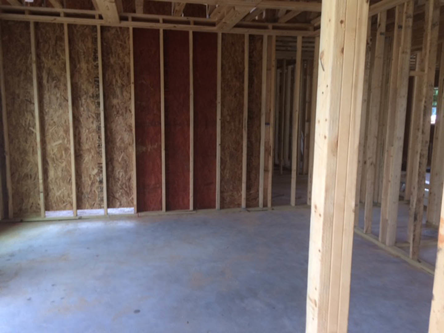 Exposed wood ceiling beams, red accent wall, concrete floor, and unfinished wooden framing in a modern interior room