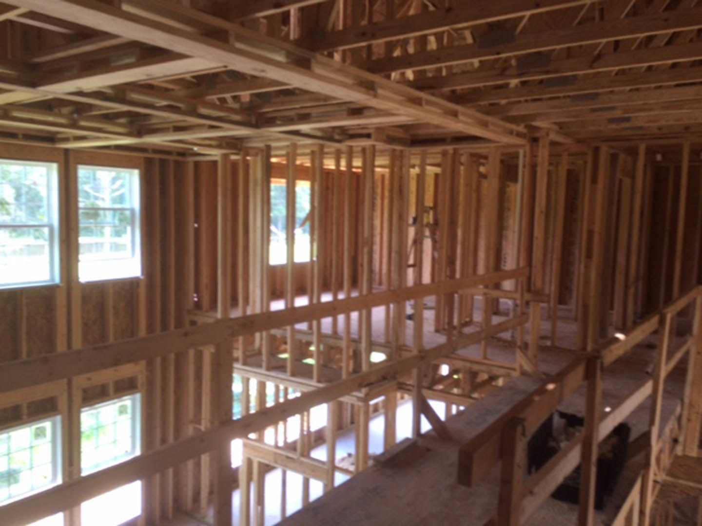 Exposed wood framing and beams with white-trimmed windows, unfinished ceiling, and natural light filtering through windows overlooking trees