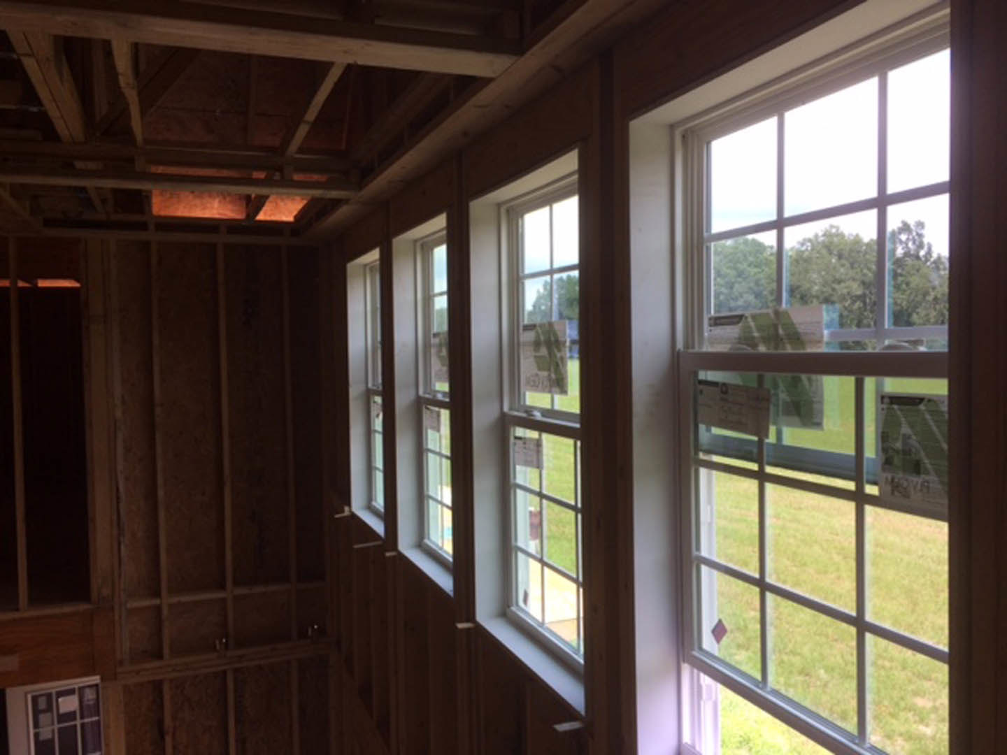 Room with wood-paneled walls, multiple large windows, views of trees and lawn outside, natural daylight illuminating hardwood finishes