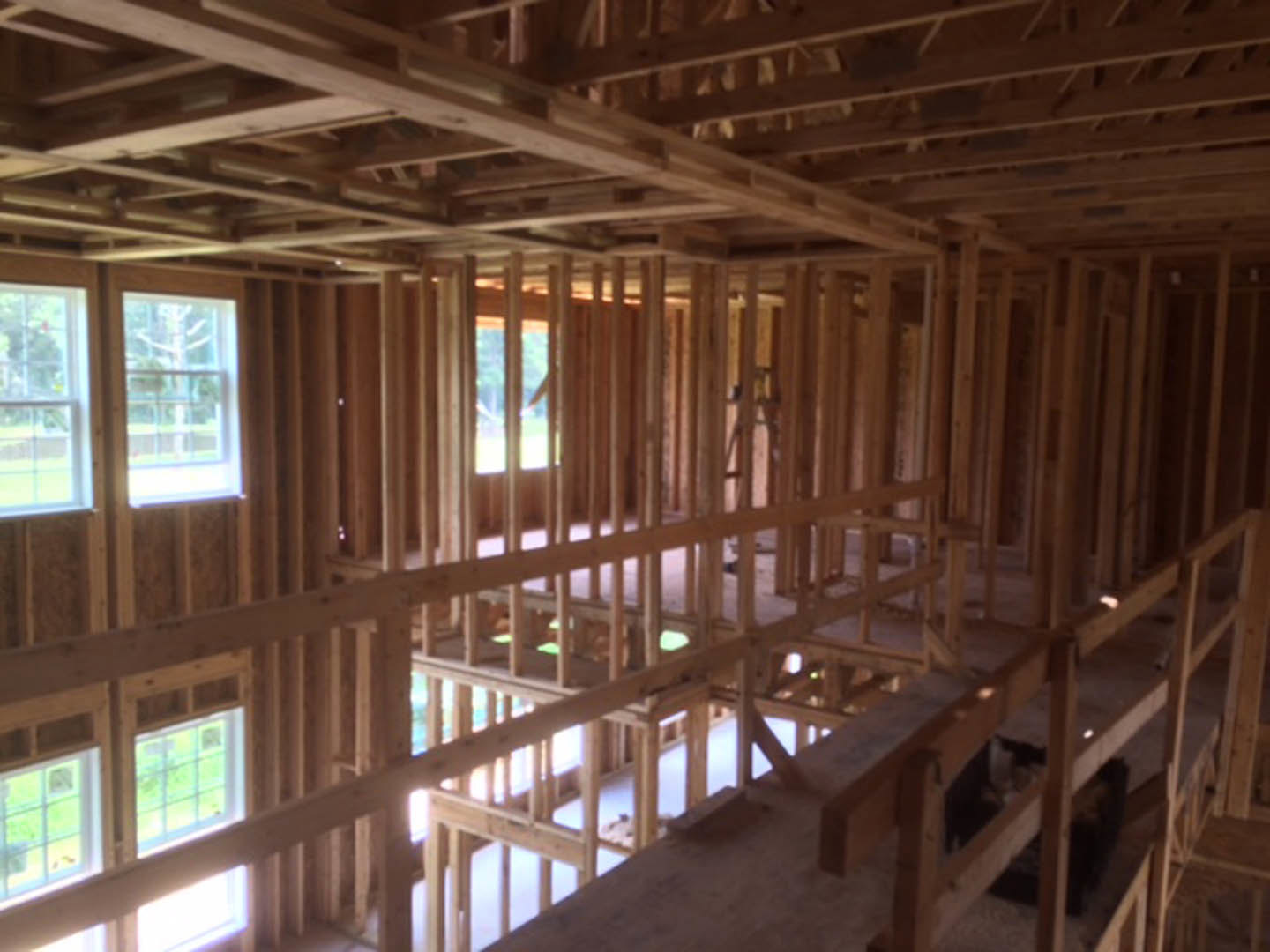 Exposed wooden ceiling beams and planks, white-framed window with tree view, unfinished wood framing in custom home interior