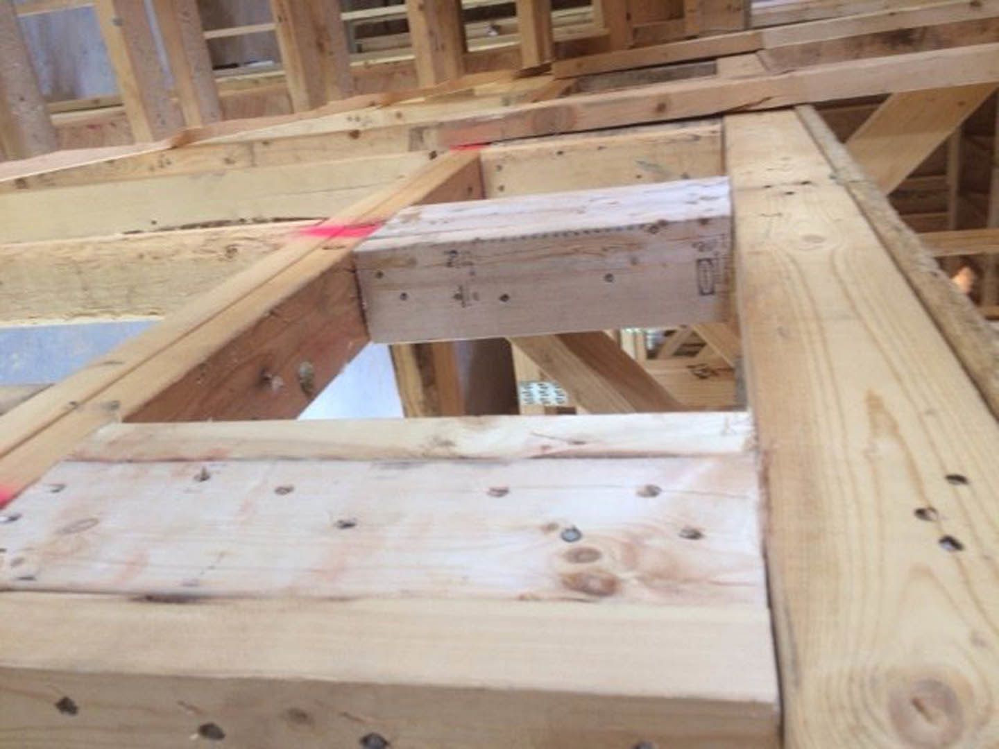 Close-up of a wooden beam with multiple drilled holes, unfinished lumber set within a residential framing structure