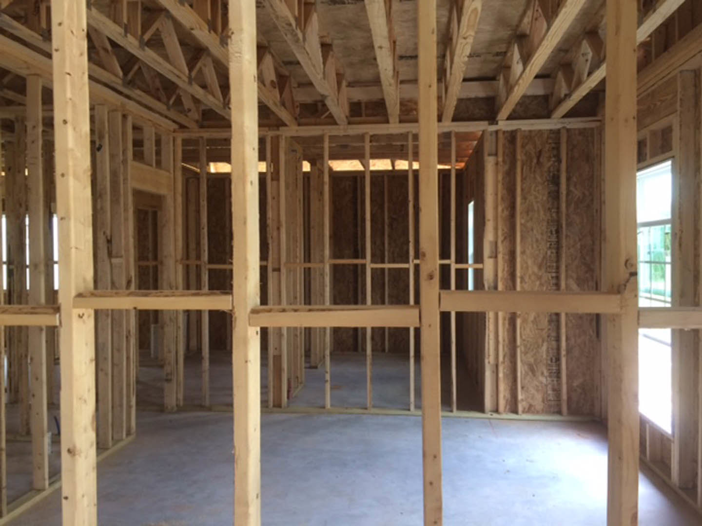 Open room with exposed wood ceiling beams, concrete floor, and large window letting in natural light; wooden framing visible along walls.