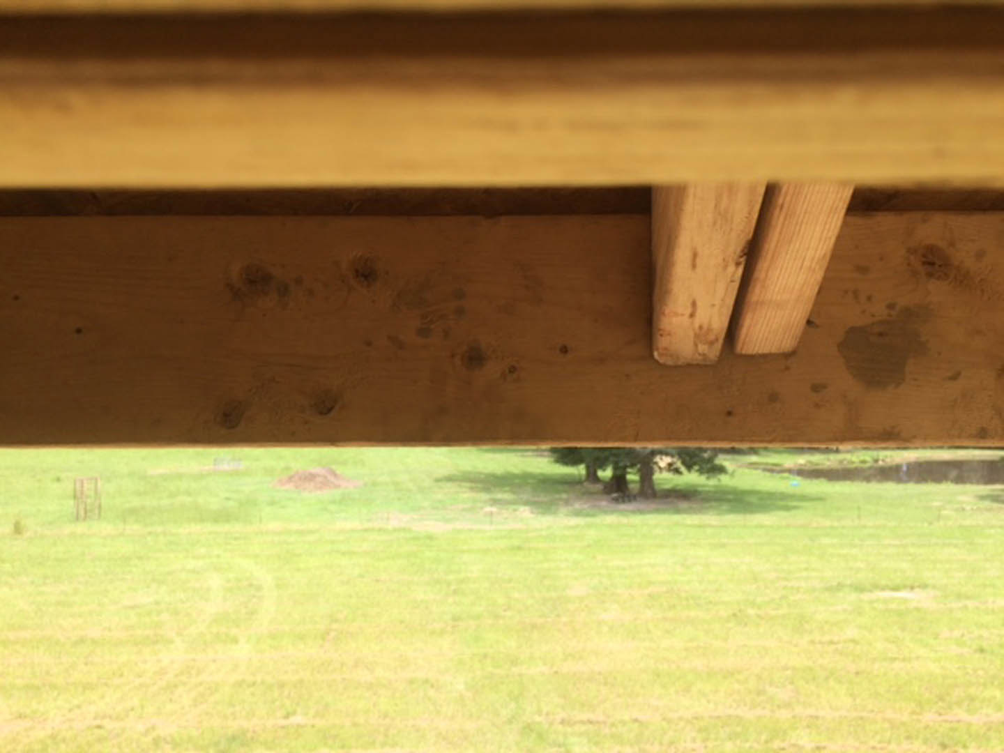 Wooden structural beam set against a green grassy field with trees in the background