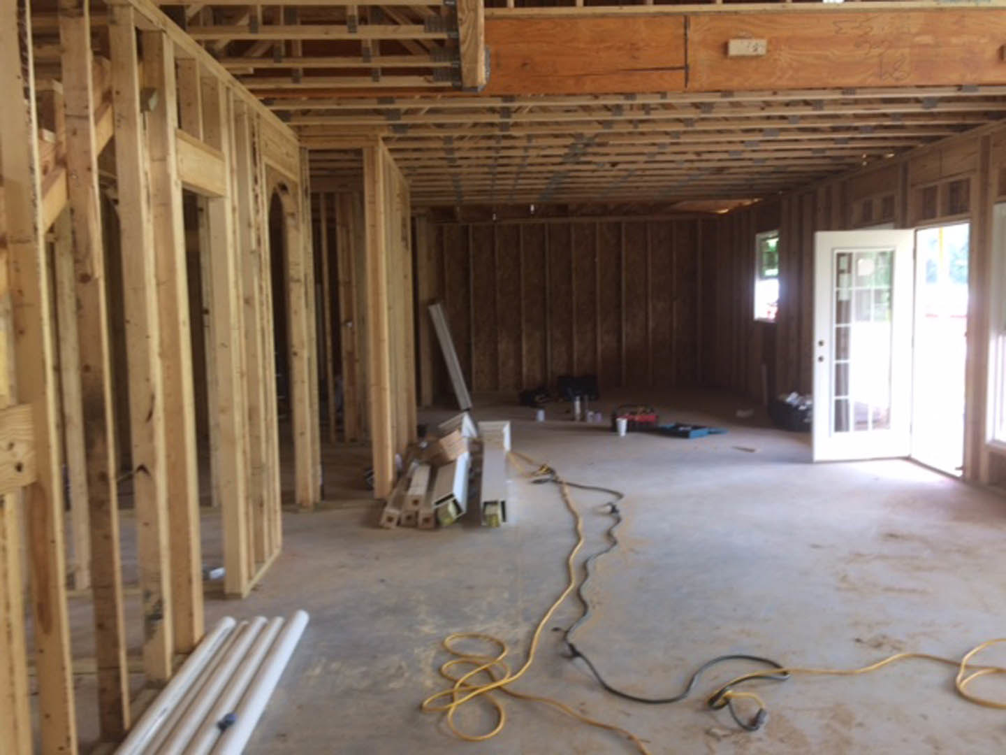 Unfinished room with exposed wood framing, white door with glass panes, ceiling beams, building insulation, and white pipes on the floor