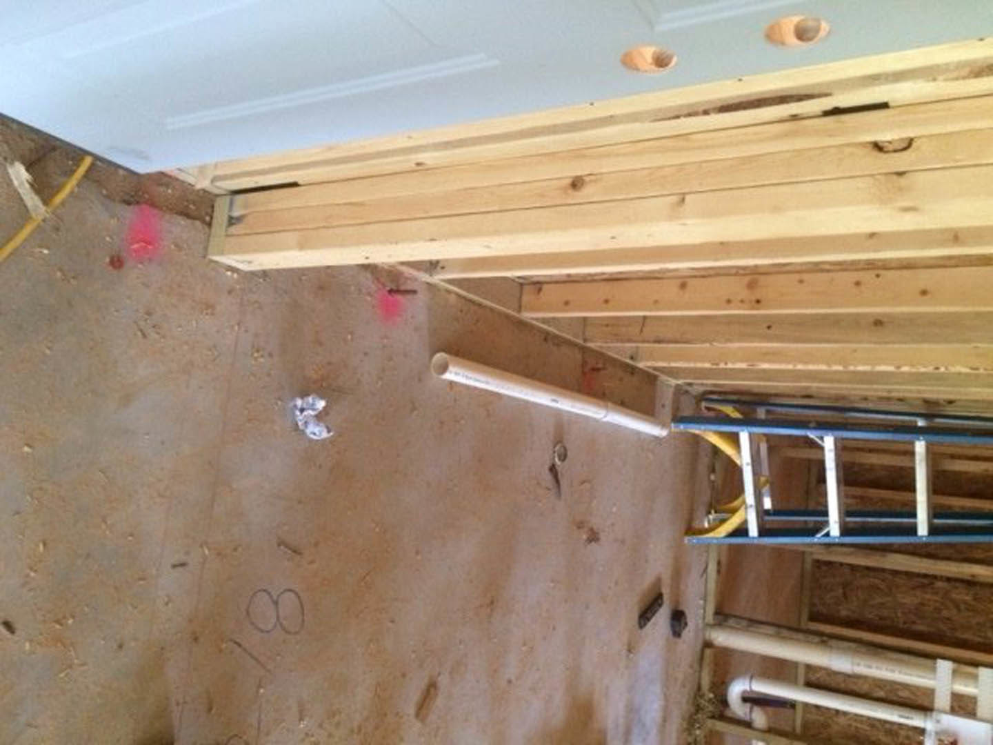 Wood ladder leaning against a plaster wall in a room with exposed beams, plywood flooring, and white railing visible in foreground