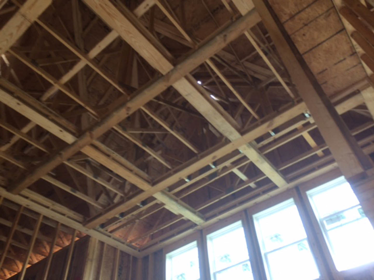 Exposed wood framing and beams on ceiling, large window with daylight streaming in, unfinished interior with visible lumber and insulation