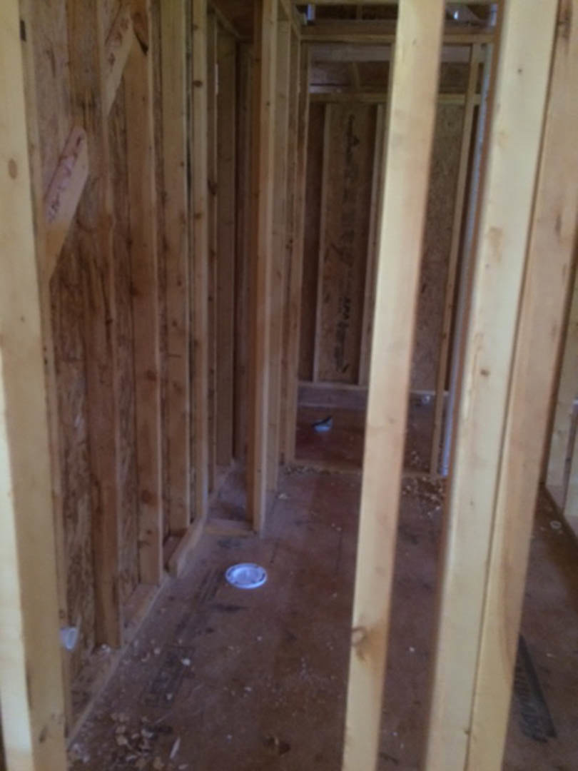 Exposed wood framing and beams inside a residential construction site, with unfinished floors and visible building insulation.