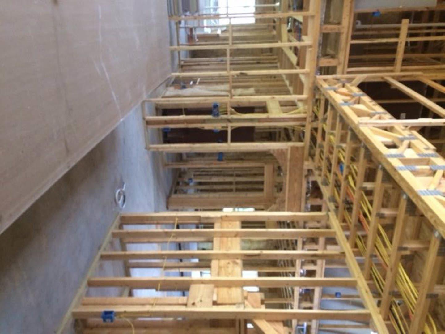 Exposed wood framing with vertical and horizontal beams, yellow straps securing lumber, unfinished interior construction