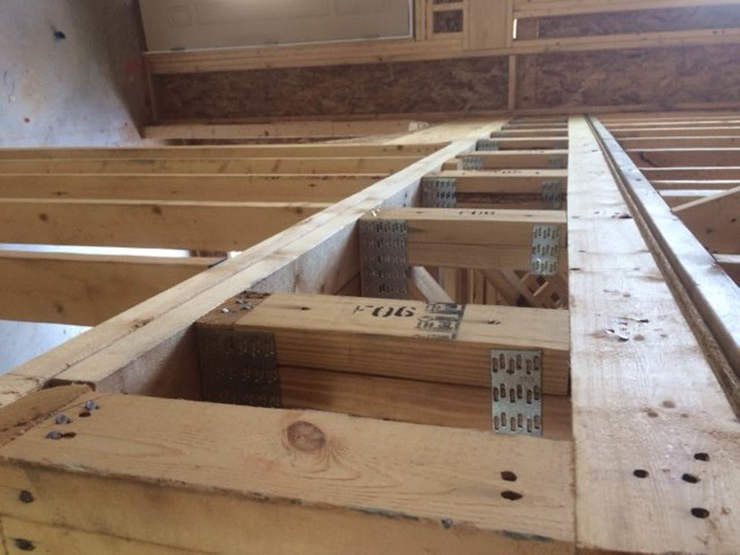 Wooden framing with metal screws, exposed beams featuring visible knots, white ceiling, brown hardwood floor, plywood and lumber materials in an unfinished indoor space