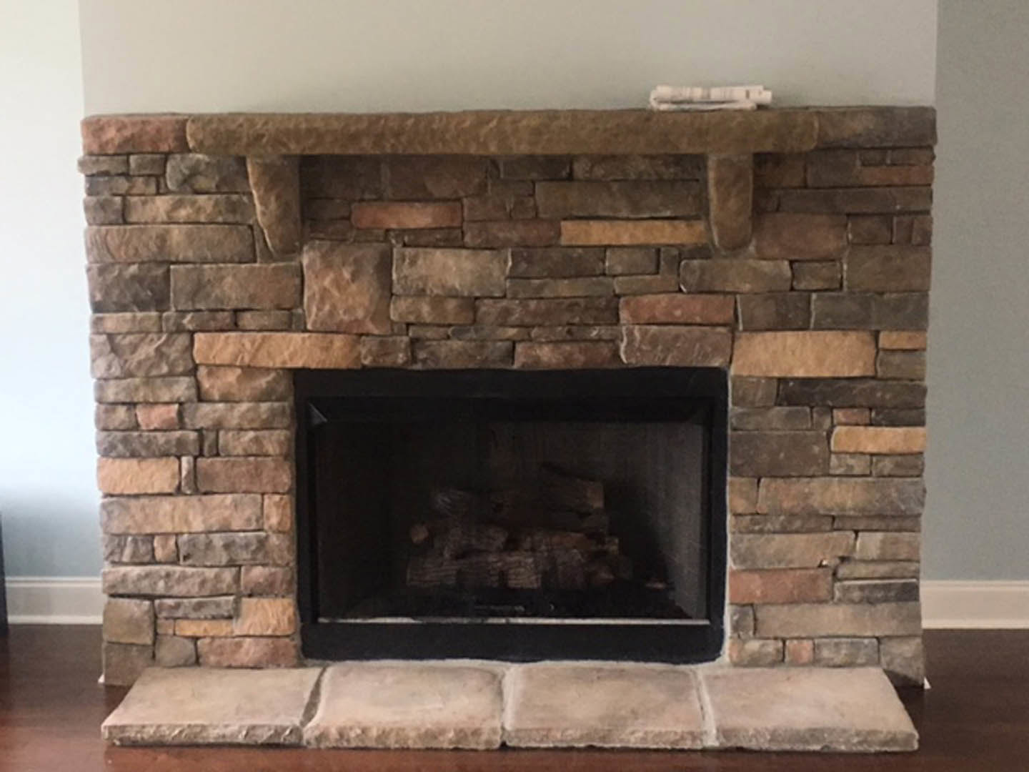 Stone fireplace with burning wood, brick hearth, fire screen, and masonry oven surrounded by indoor stone wall