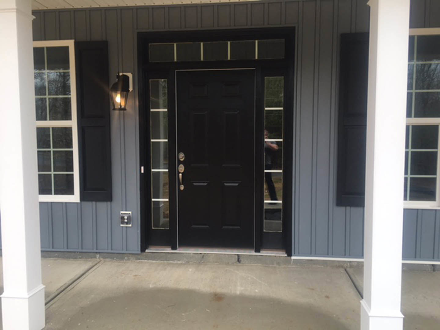 Black front door with glass panes and silver handle set in white siding, adjacent to a window