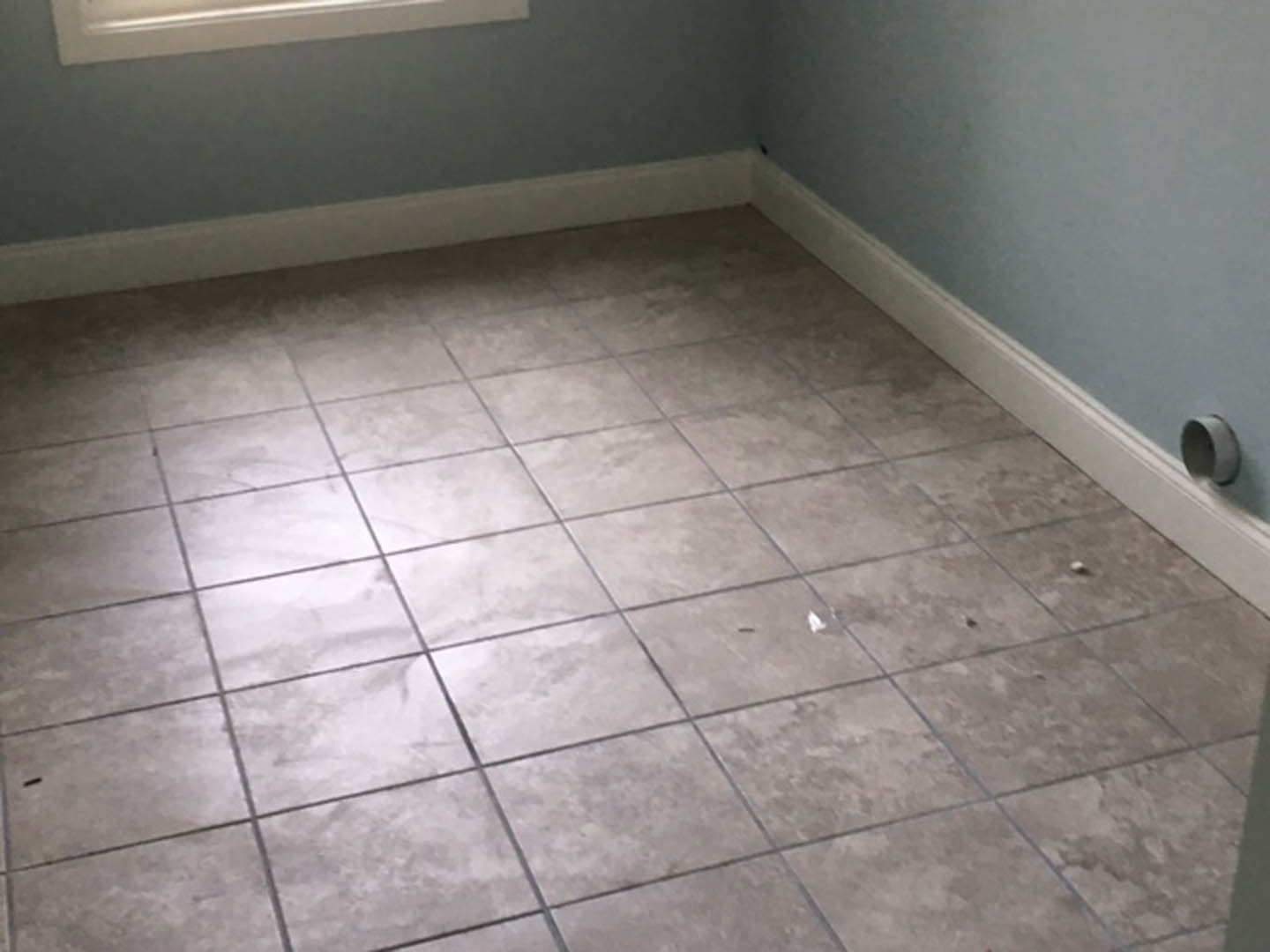 Close-up of light-colored tile flooring with white baseboard trim and white plaster wall in a bathroom interior