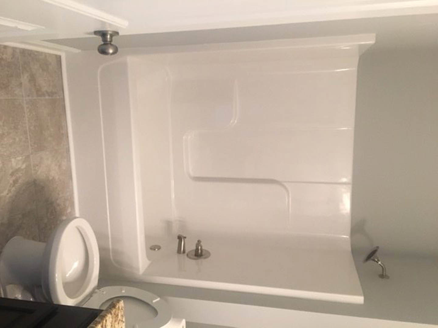 White bathtub with chrome faucet beside a toilet with open seat, surrounded by light tile walls and floor in a modern bathroom.