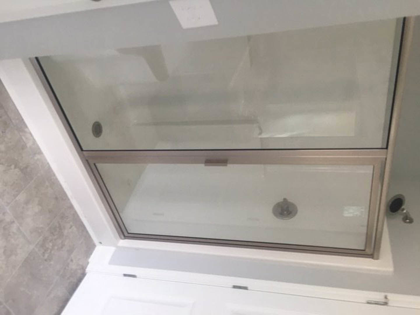 Walk-in shower with clear glass door, white tile walls, chrome fixtures, and partial view of a white bathtub and sink