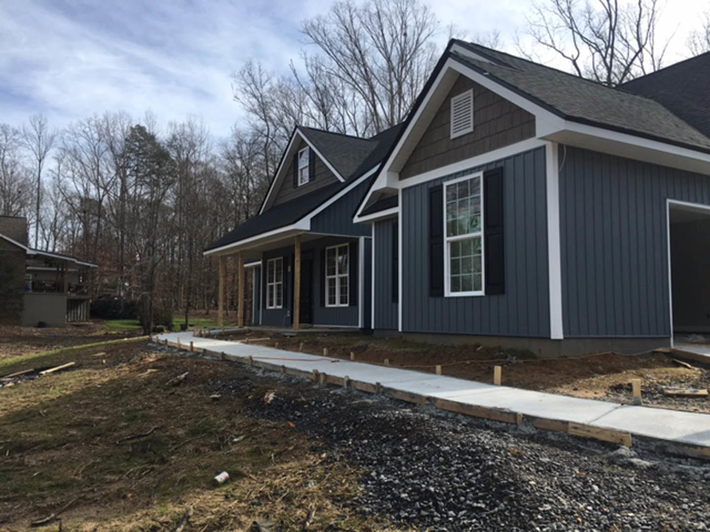 Two-story house with gray siding, white trim windows, and a concrete walkway leading through landscaped front yard with mature trees