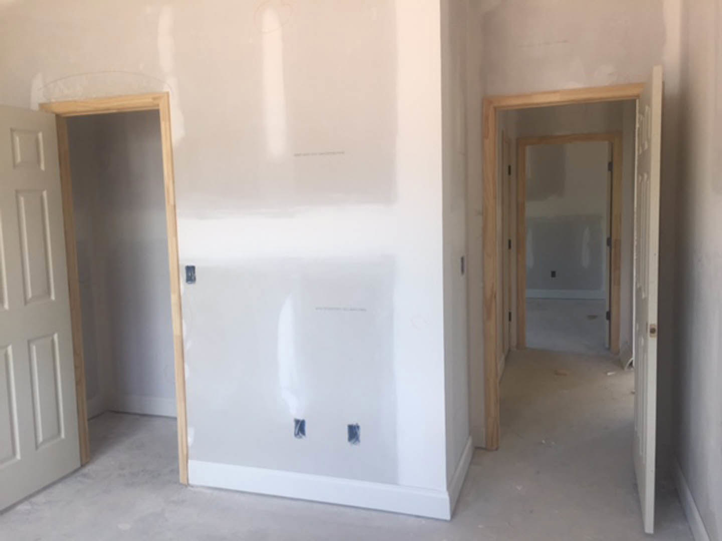 White-walled room with light wood flooring, white door, and simple trim detailing