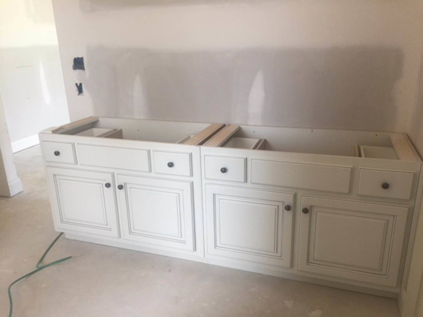 White kitchen cabinets with drawers and round knobs, green wire on the floor, white fabric with black stripe, close-up of cabinetry against wall