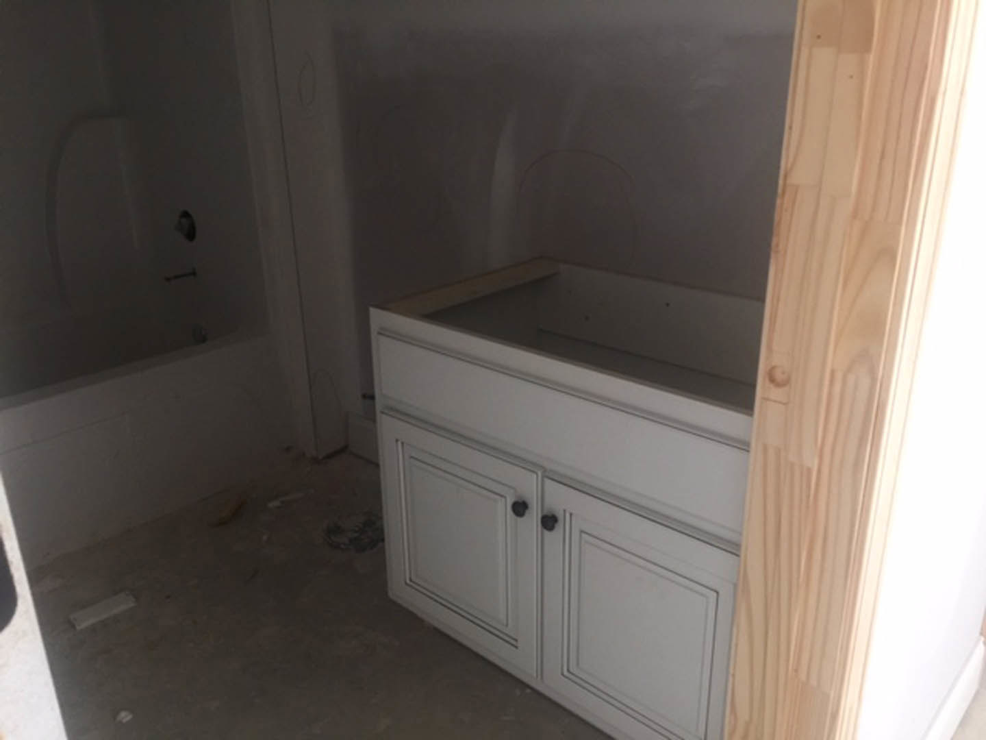 White bathroom with freestanding tub, white sink cabinet with black knobs, wood door frame, tile floor, and red wall accent.