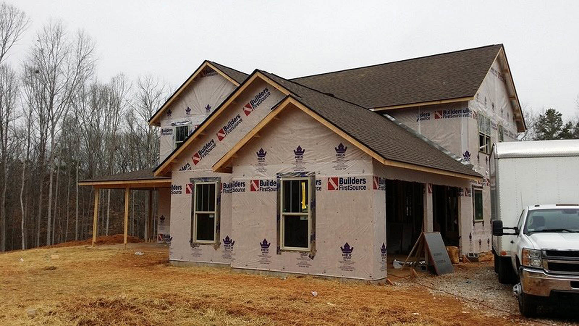 Partially built house with exposed insulation, several installed windows, and a white pickup truck parked in front