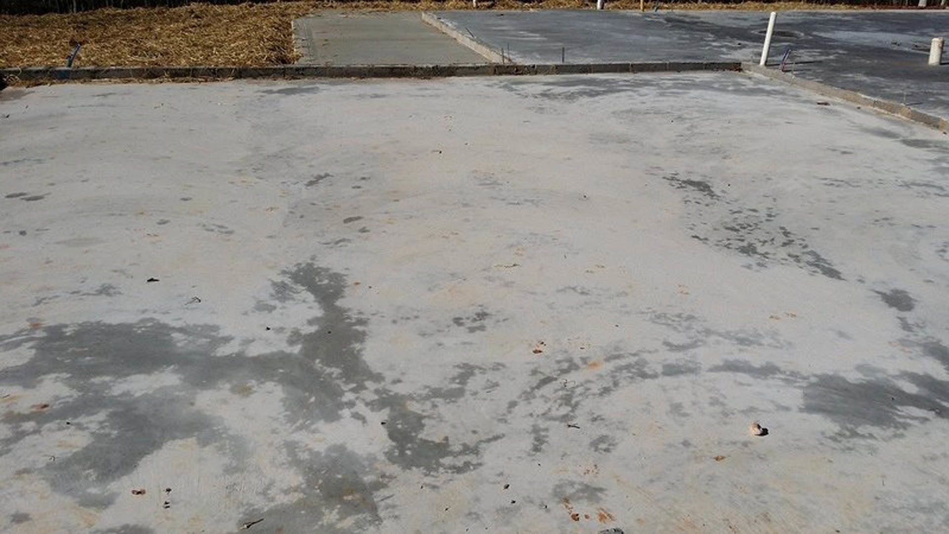 Smooth concrete slab foundation with several smaller concrete slabs resting on top, surrounded by outdoor ground.