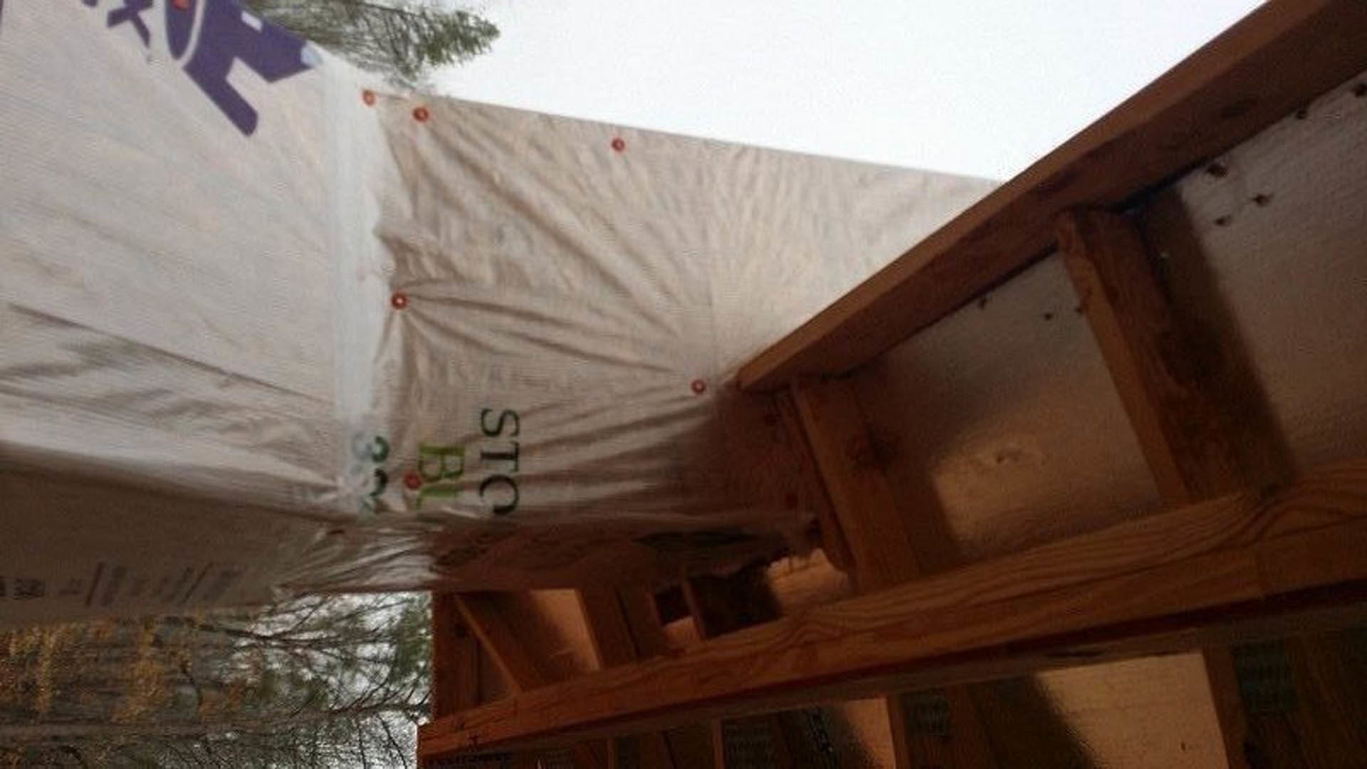 White plastic bag resting on a wooden table inside a partially constructed home with exposed wood framing and visible window openings.