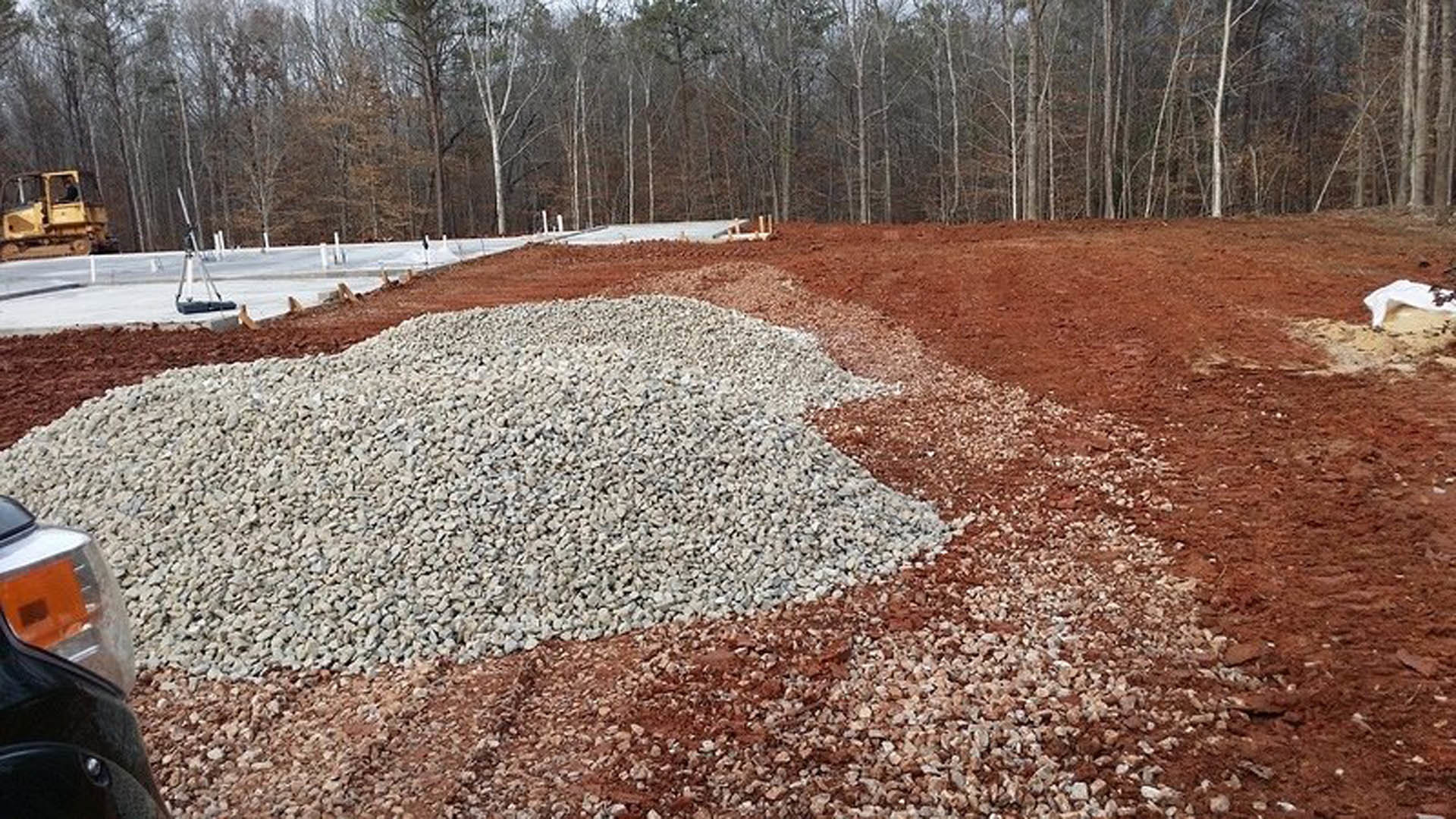 Large pile of gray rocks on bare dirt field with scattered trees in background under overcast sky