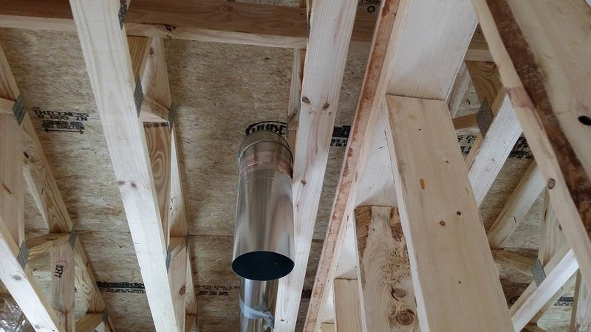 Exposed metal pipe running through unfinished wood framing with visible lumber beams and building insulation