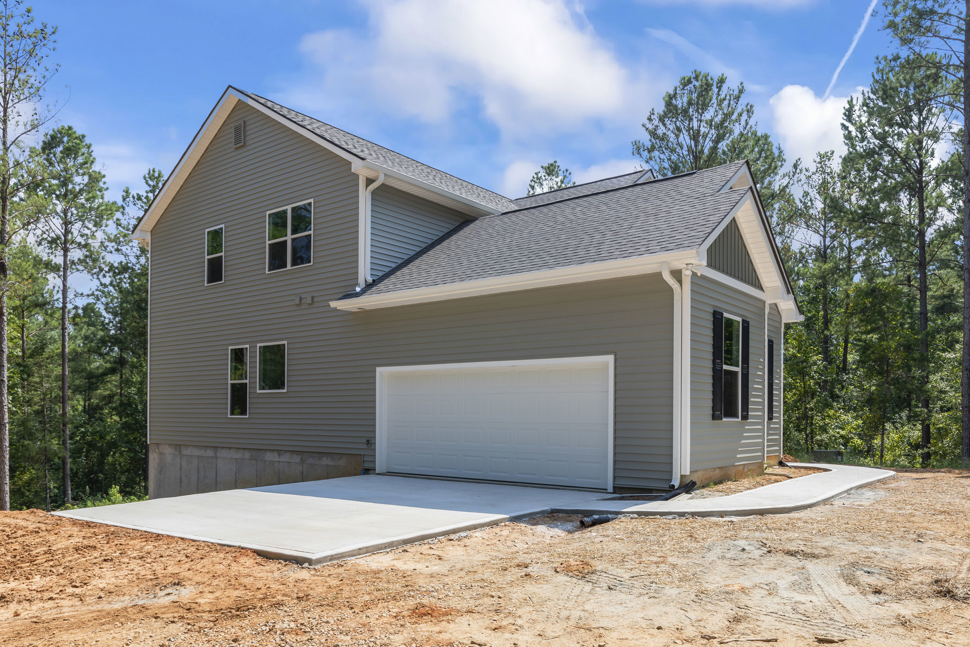 Two-story house with gray roof, white siding, attached garage, white gutter, green-tinted window, and concrete driveway bordered by dirt.