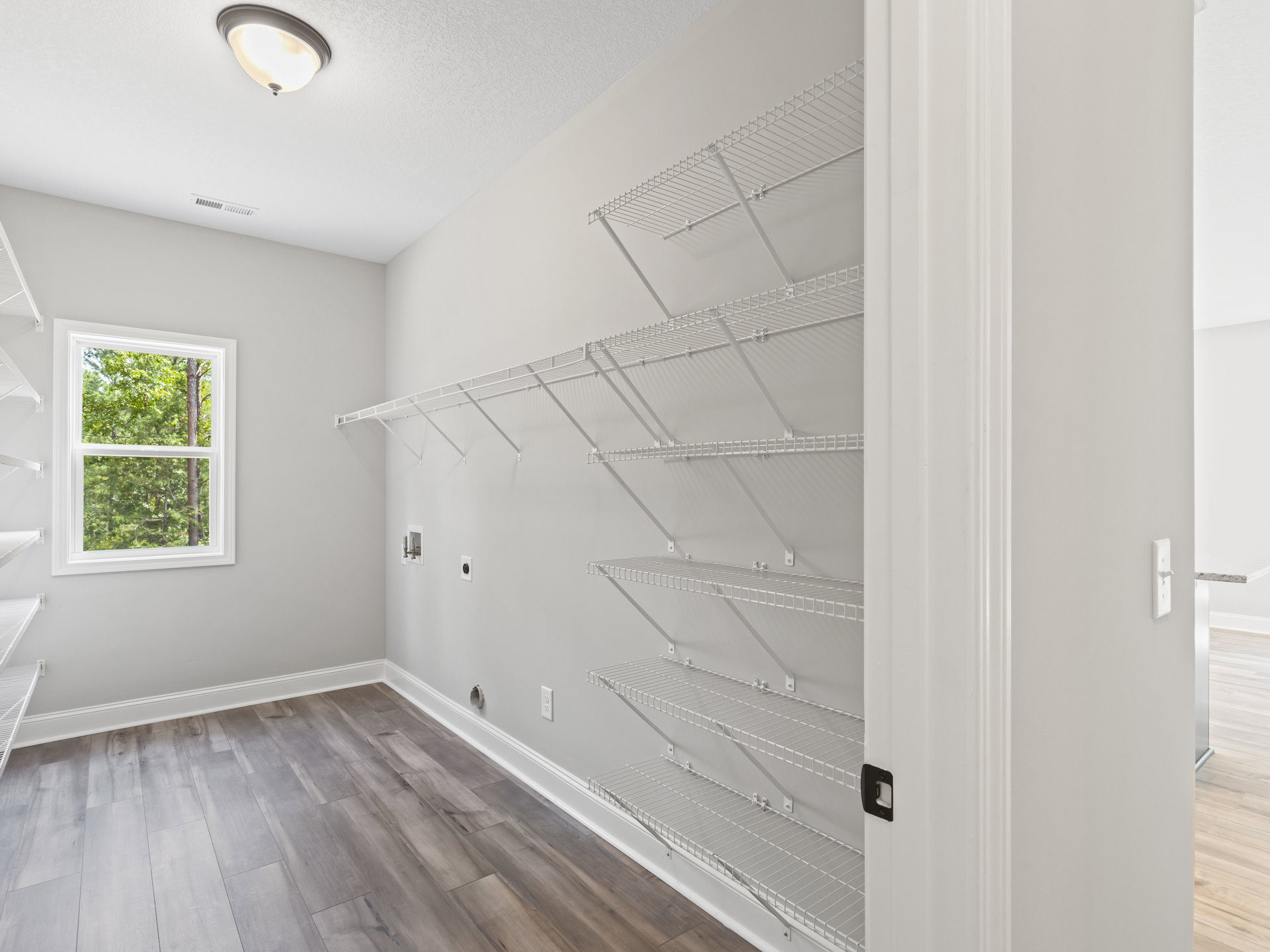 Hardwood floor room with built-in white shelves, window overlooking trees, ceiling light fixture, and wall opening