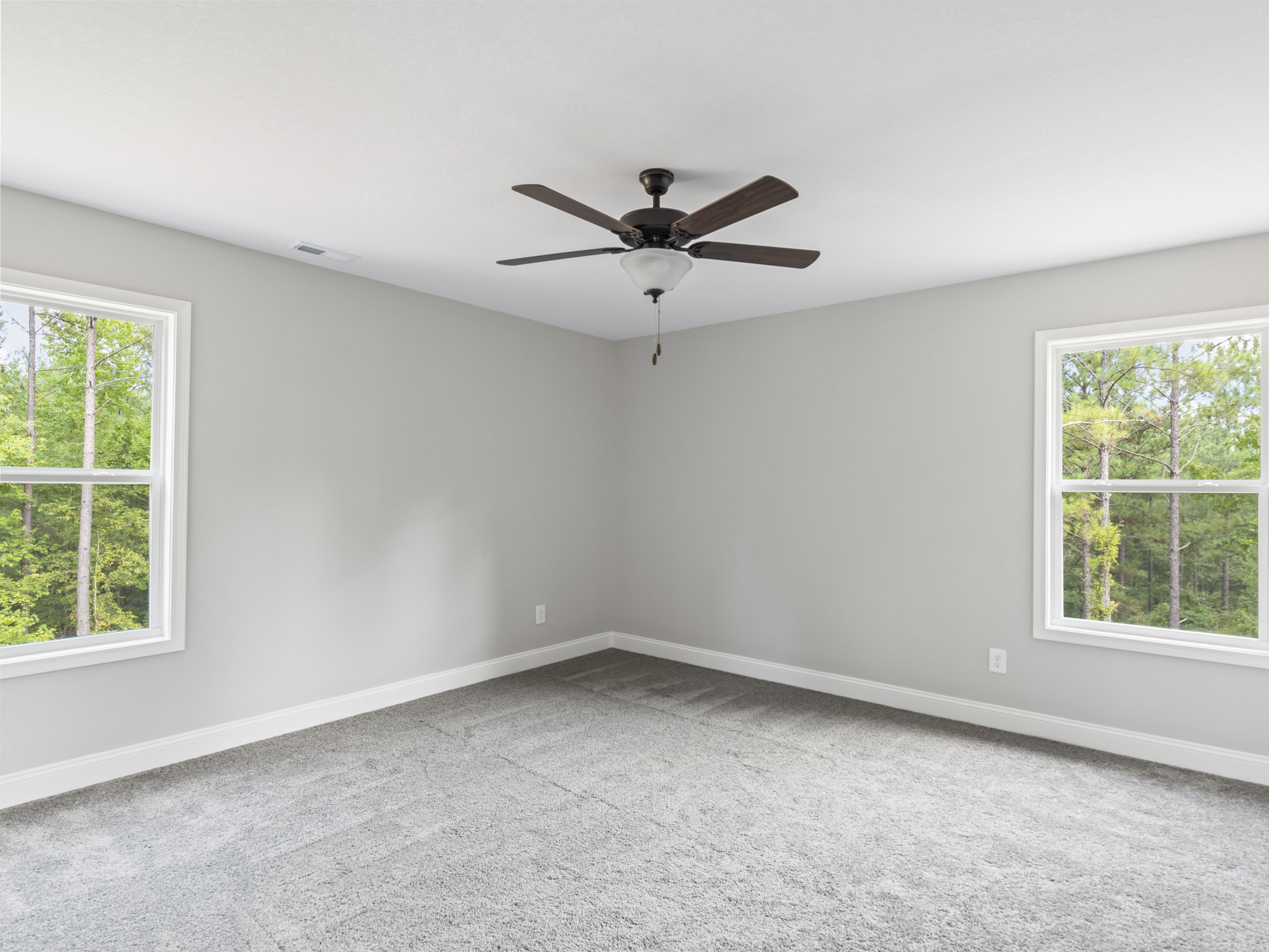 Carpeted room with white walls, ceiling fan with light fixture, large windows showing leafy trees outside
