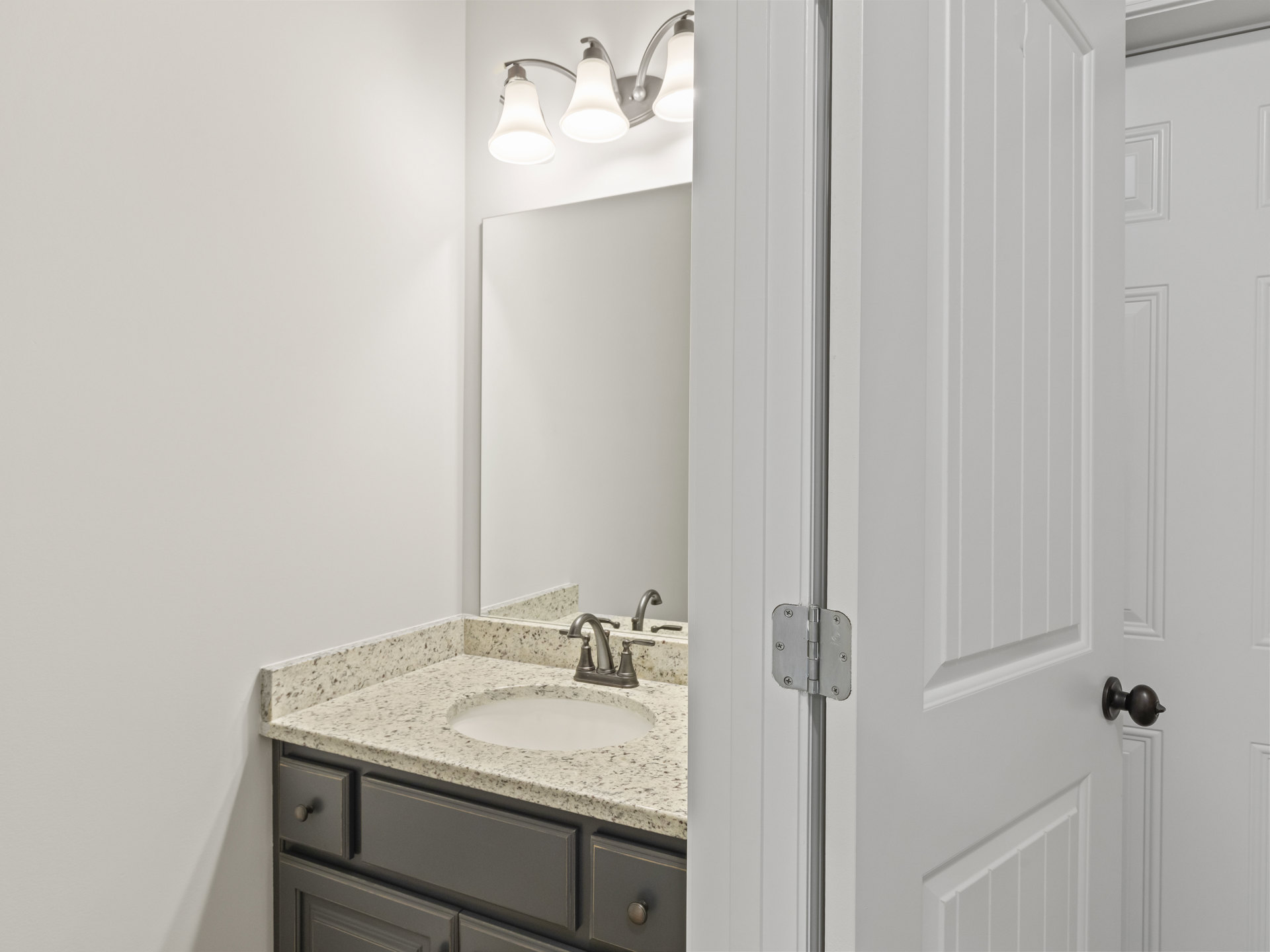White bathroom vanity with shaker cabinets, chrome faucet, rectangular undermount sink, quartz countertop, large framed mirror, three-light wall sconce, and neutral tile backsplash