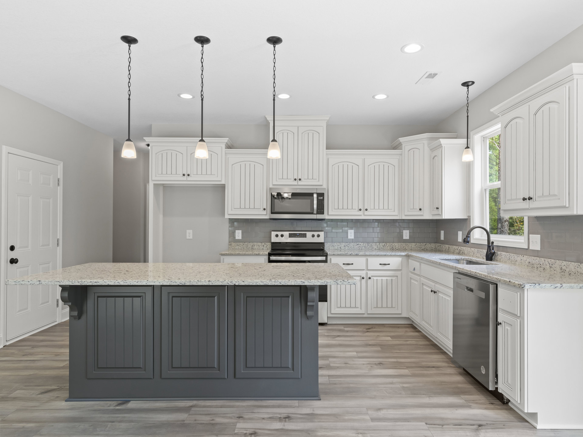 White kitchen cabinets with granite countertops, stainless steel oven and microwave, modern pendant lighting, and undermount sink