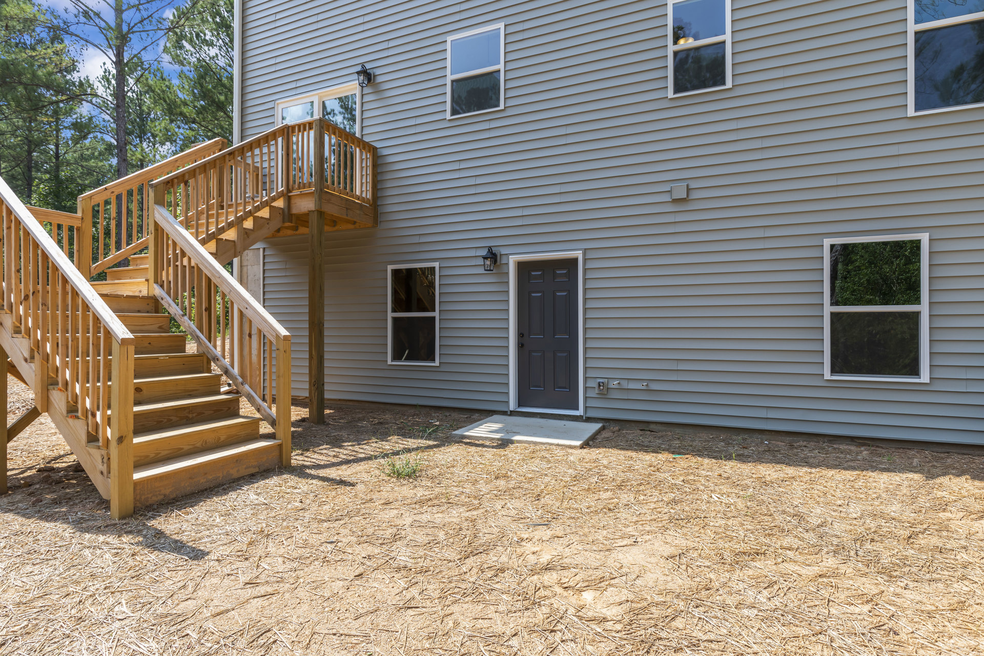 Two-story home exterior with white siding, black front door framed in white trim, wooden staircase leading to porch, large windows reflecting trees, metal handrail along stairs