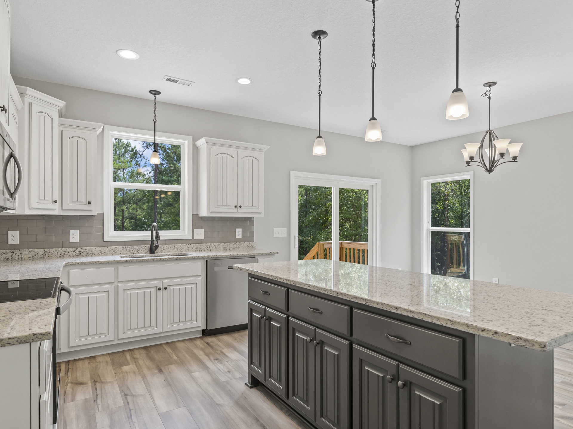 White kitchen with shaker cabinets, marble island countertop, stainless steel sink, pendant lights with black metal chains, and large window providing natural light.