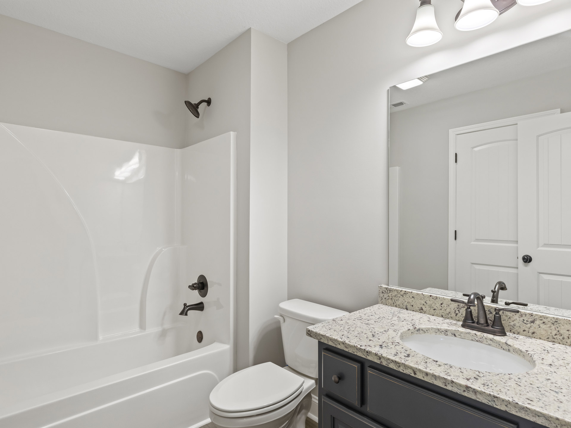 Modern bathroom featuring a white toilet, wall-mounted shower head, rectangular sink with chrome faucet, light fixture with white shade, and neutral tile finishes.