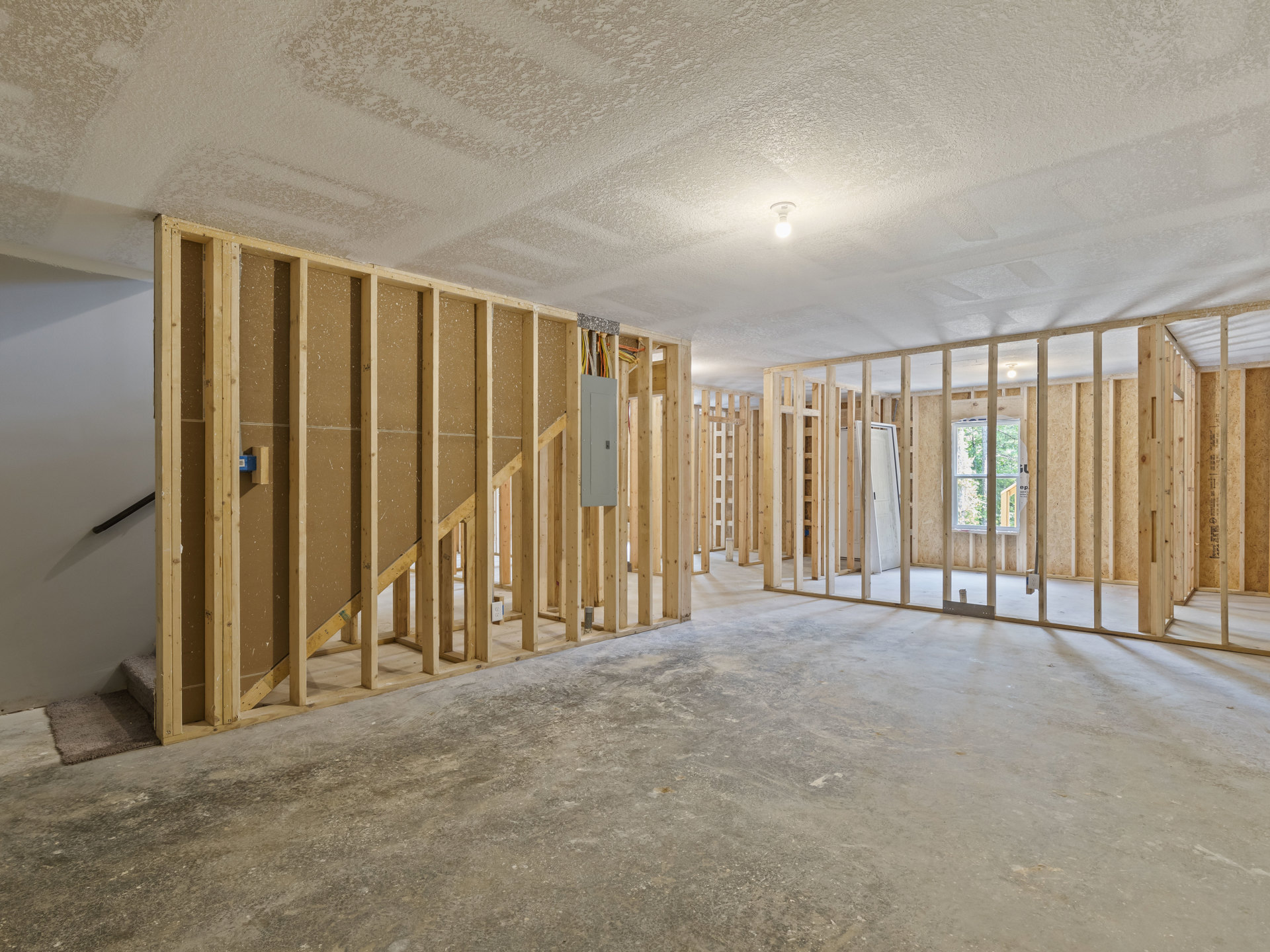 Beige plaster wall and staircase in a room with concrete floor, exposed wood beams, ceiling light fixture, and built-in shelf