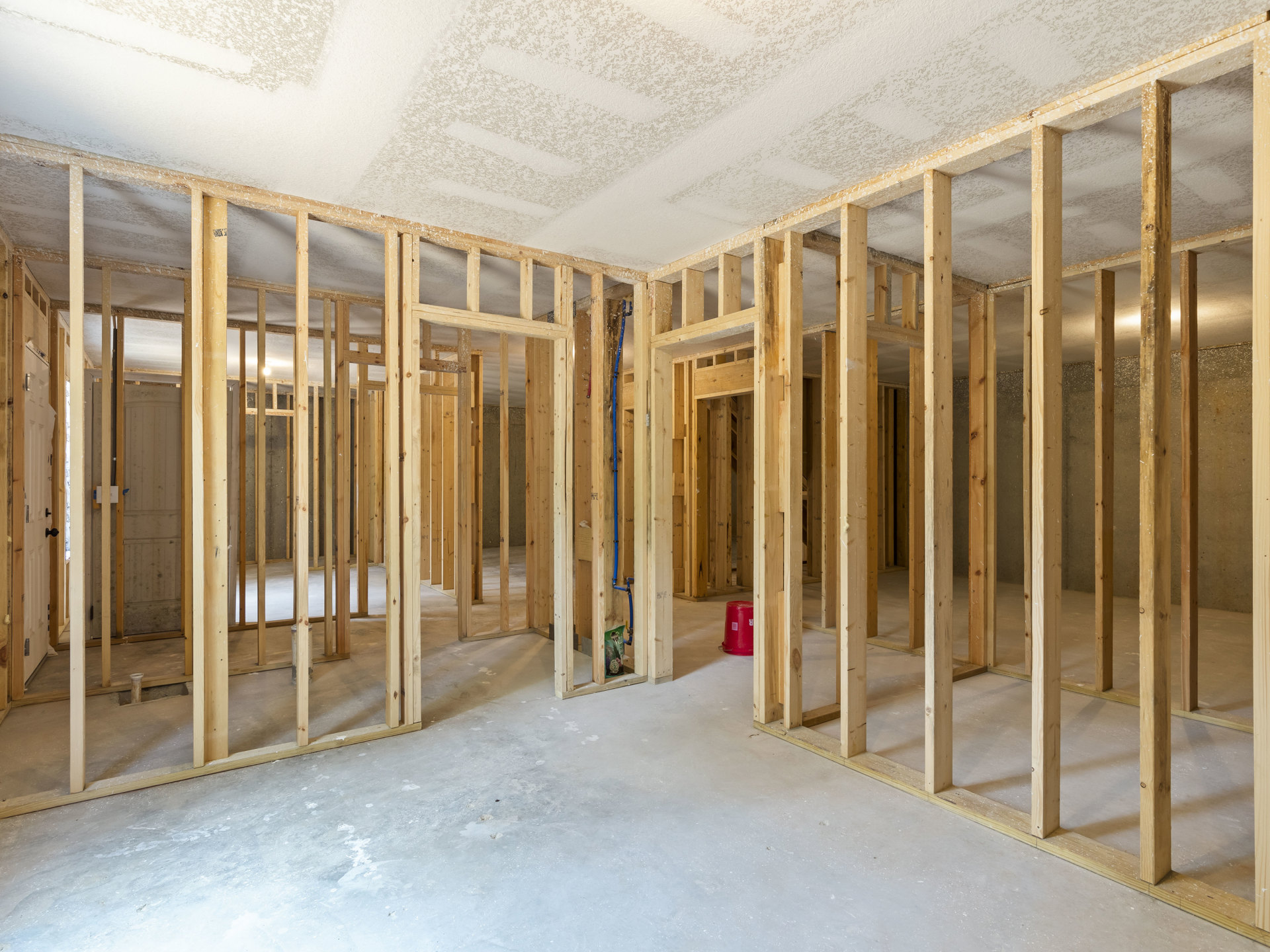 Room under construction with exposed wood framing, patterned white ceiling, wood beams, and red bucket on unfinished floor