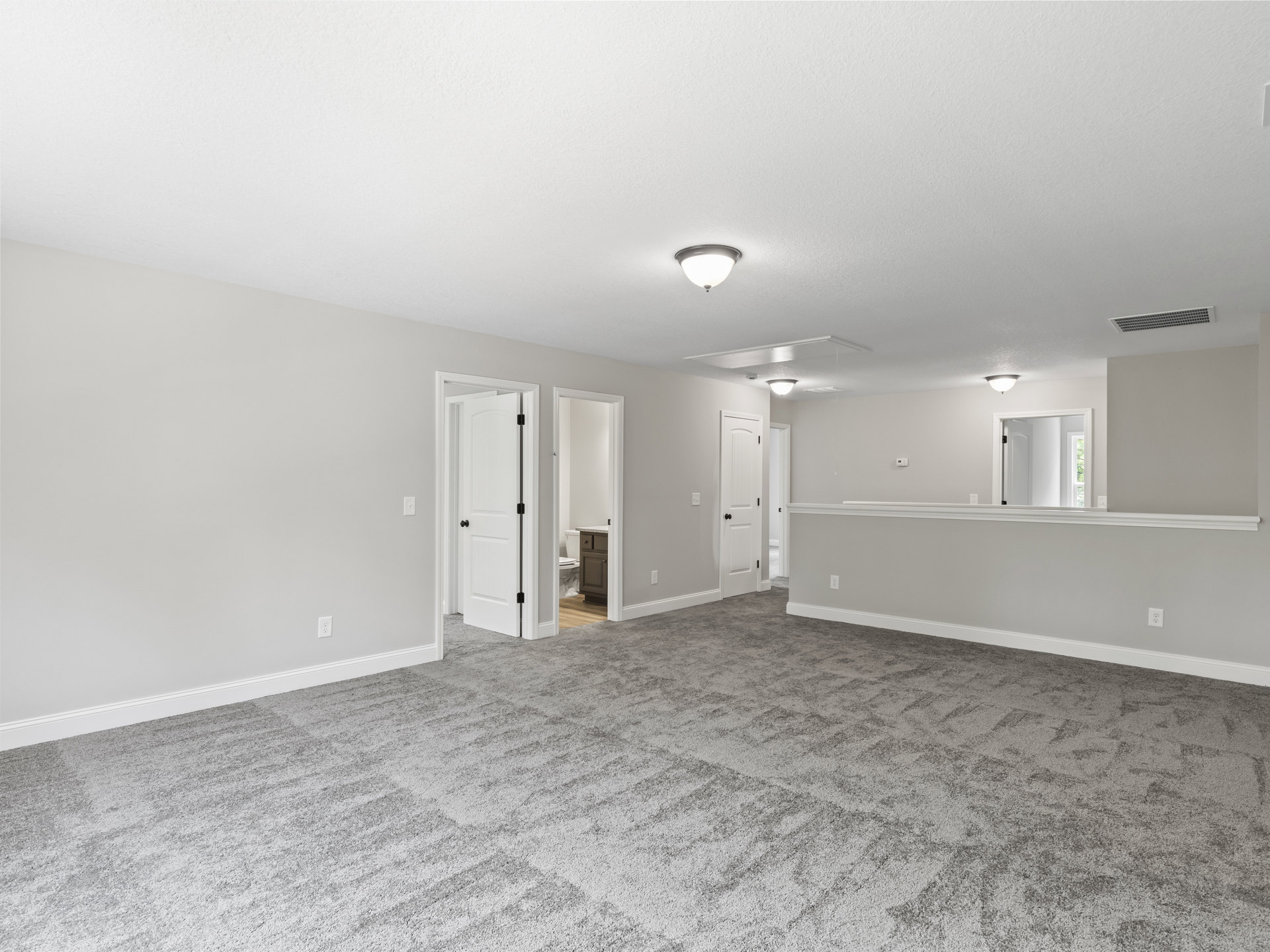 Carpeted room with white plaster walls, open white door featuring black hardware, and ceiling light fixture