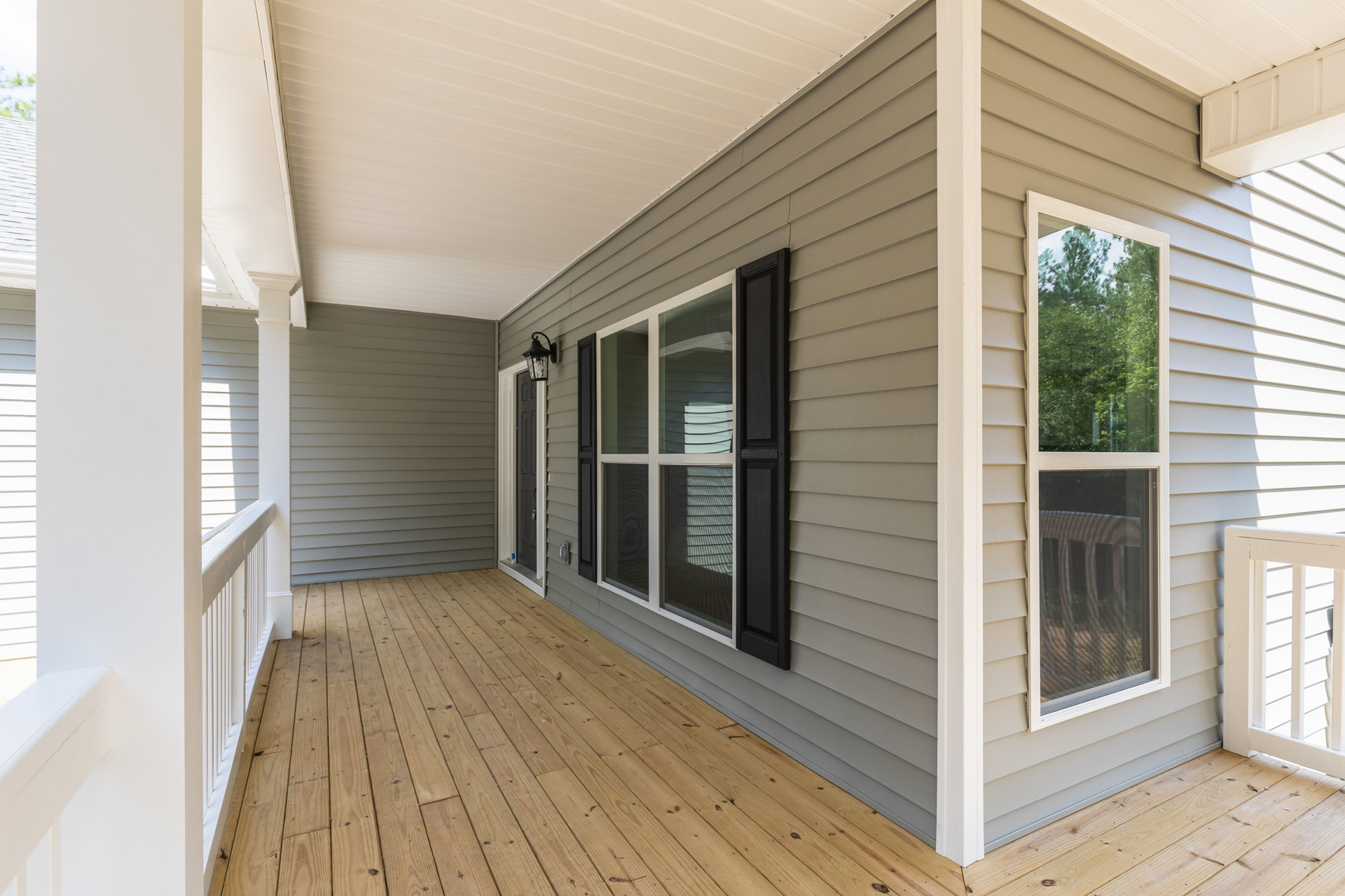 Two-story home with wood deck, glass door with black shutter, white window with blinds, surrounded by trees