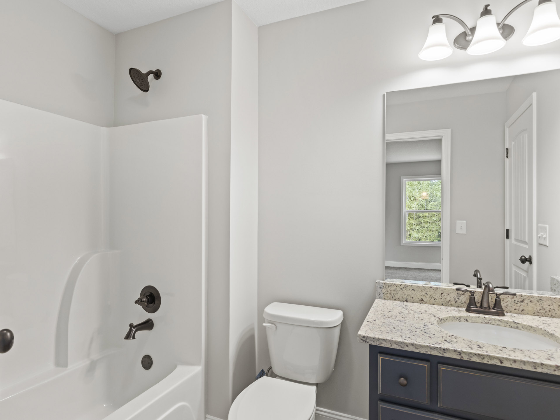 Bathroom with white toilet and rectangular sink, wall-mounted light fixture, round shower head, tiled walls, window showing green trees outside