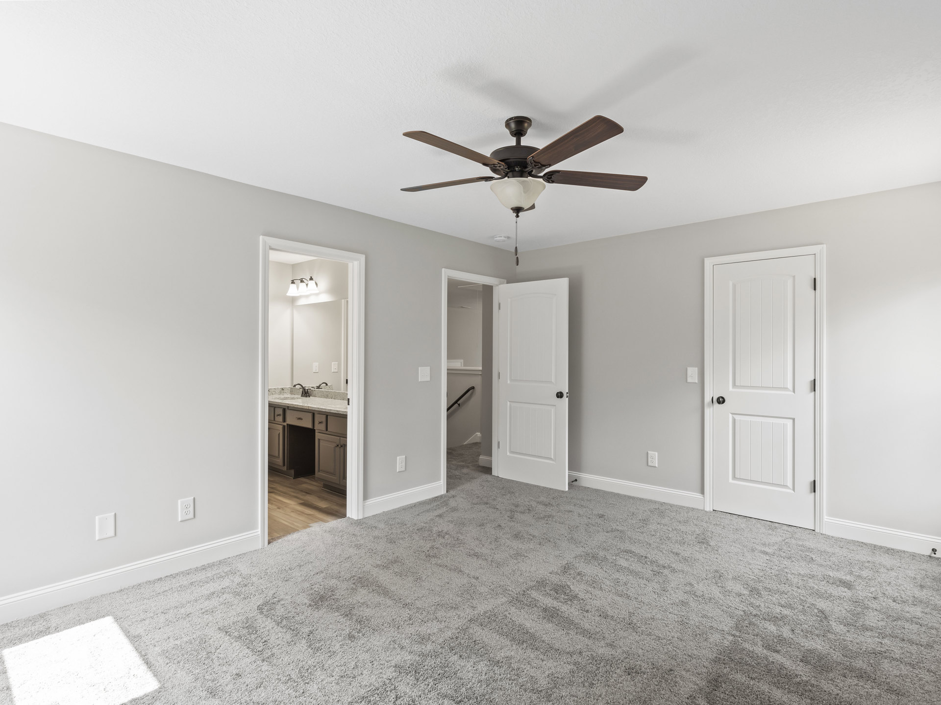 Ceiling fan with light fixture, two white doors with black knobs, black handrail mounted on wall, white carpeted floor with square pattern