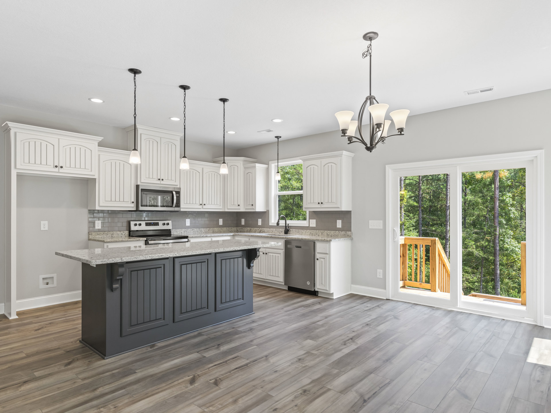 Spacious kitchen featuring a large central island with quartz countertop, wood plank flooring, white cabinetry, stainless steel appliances, and undermount sink