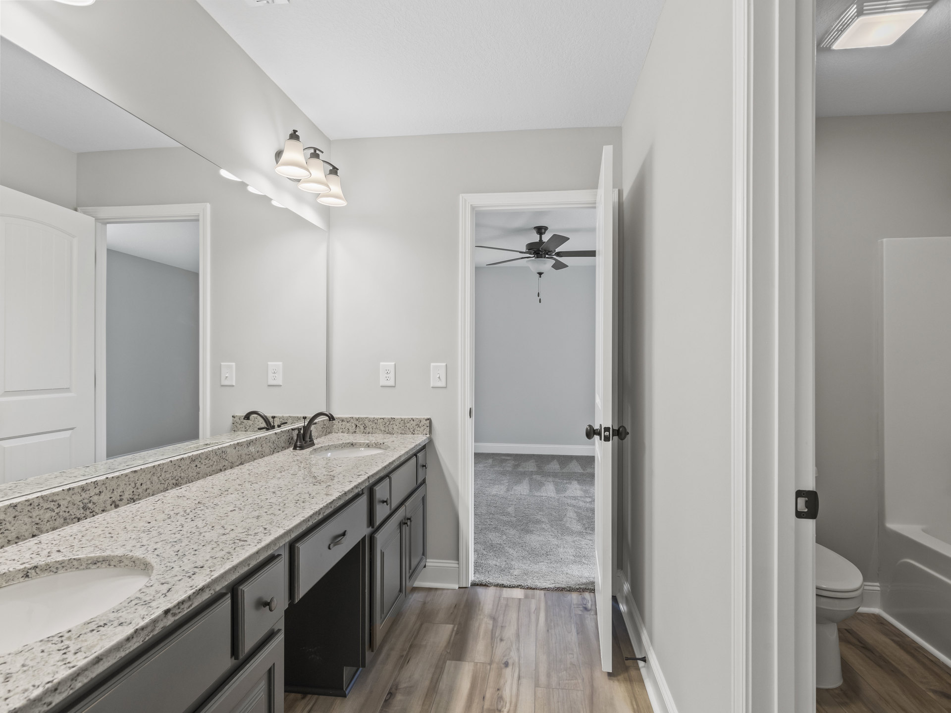 Bathroom featuring a marble countertop, wood flooring, white cabinetry, undermount sink, three-light fixture above mirror, ceiling fan with light, and closed toilet seat