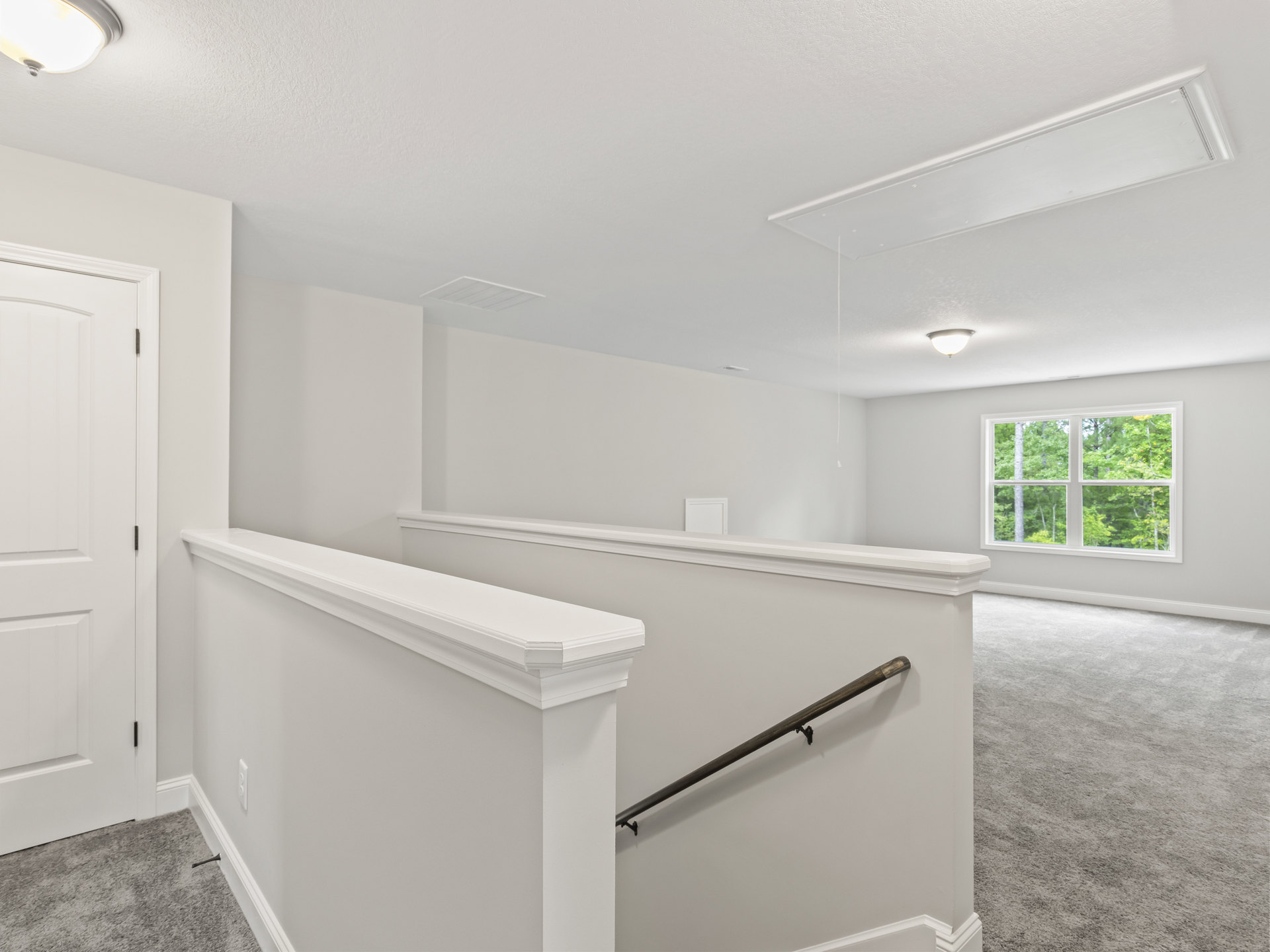 White carpeted stairs in a bright room with white walls, a window showing trees outside, white door with black hinge, built-in white shelf, metal pole with clip, and close-up of a