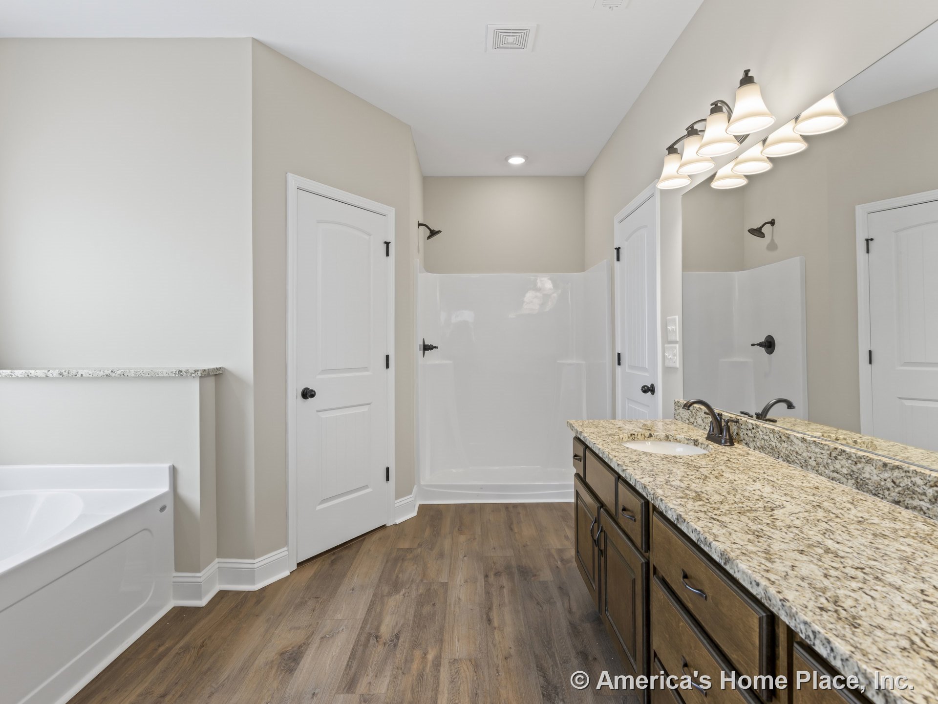 Double vanity with granite countertops and cabinetry, walk-in glass shower enclosure, wood-look plank flooring, large wall mirror, built-in overhead lighting, white paneled doors