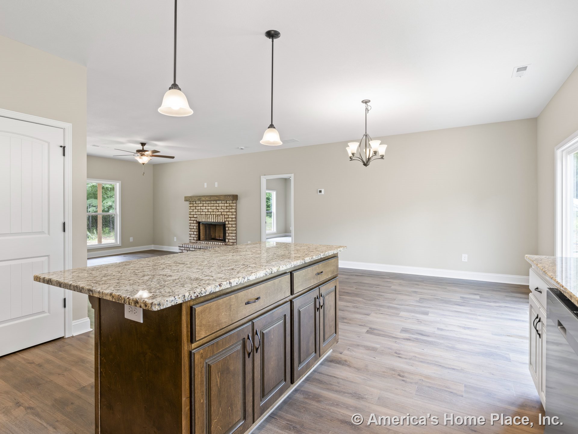 Granite kitchen island with wood cabinetry, pendant lighting, and brick fireplace in open floor plan; large windows and wood-look flooring throughout.