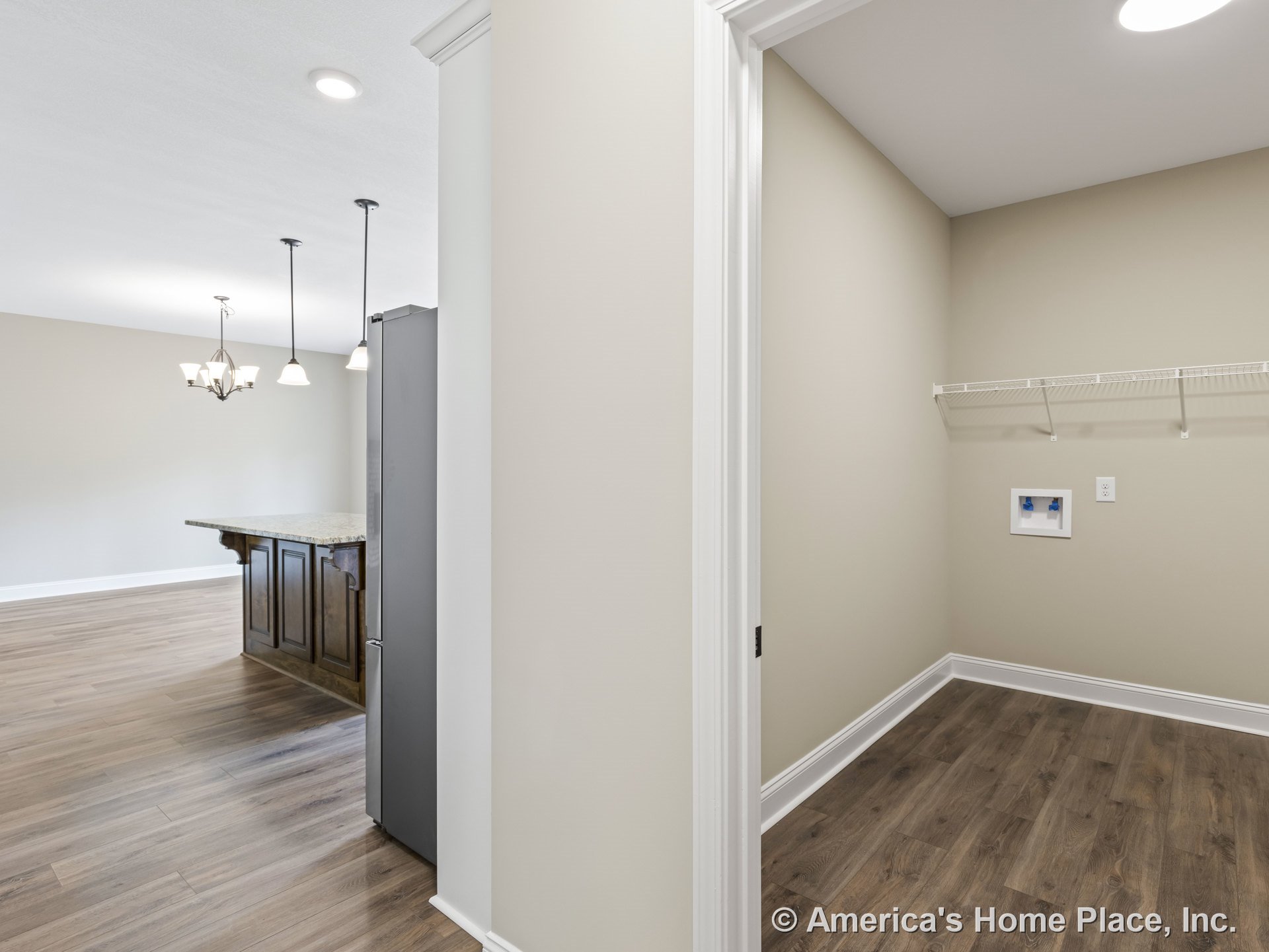 Laundry room with wire shelving and wall utility hookups next to open kitchen featuring granite island, pendant lights, wood-look flooring, baseboard trim, recessed lighting, and