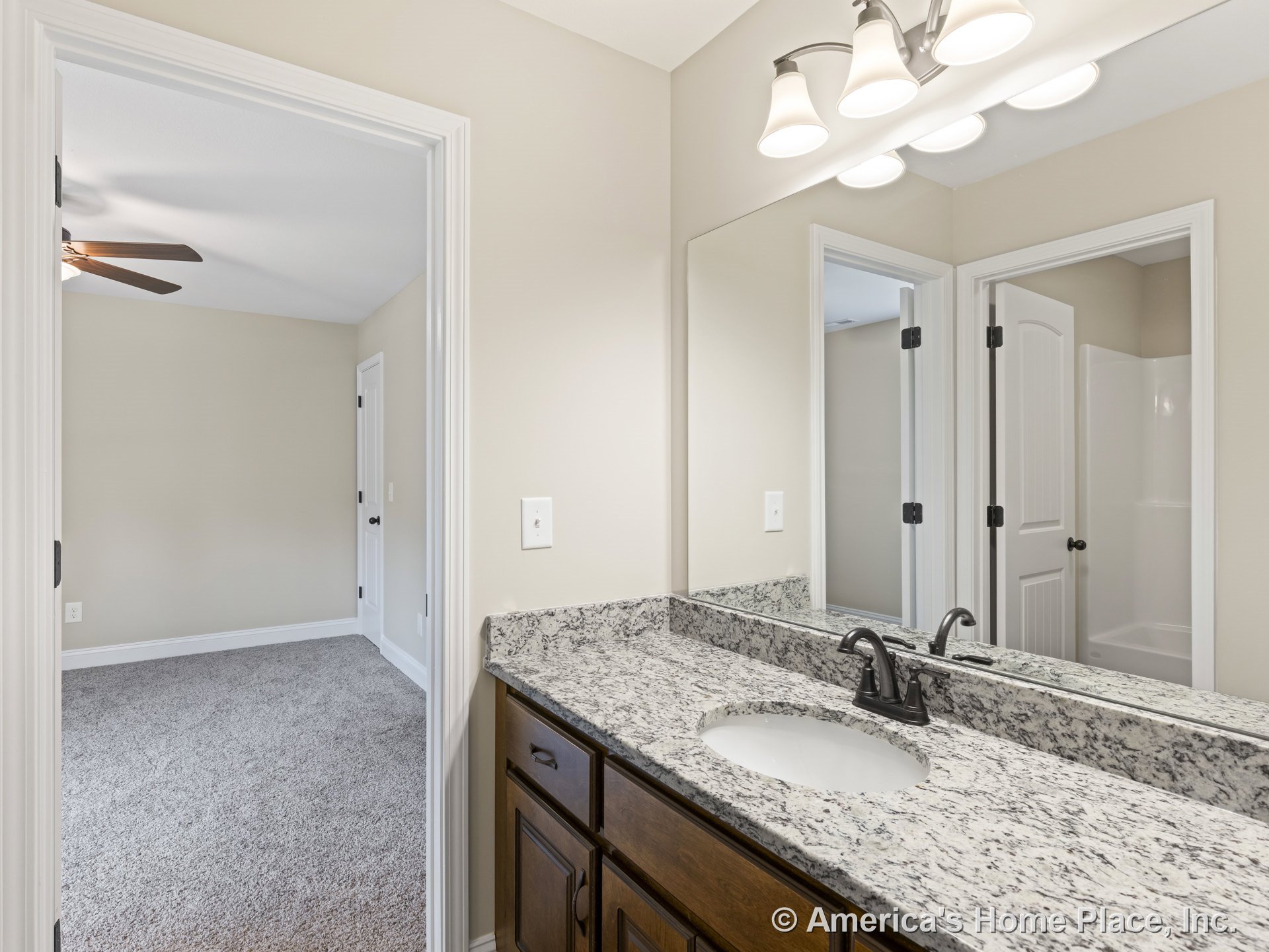 Granite bathroom vanity with undermount sink, dark wood cabinetry, large wall mirror, three-light fixture, white trim and doors, carpeted adjacent bedroom visible through open